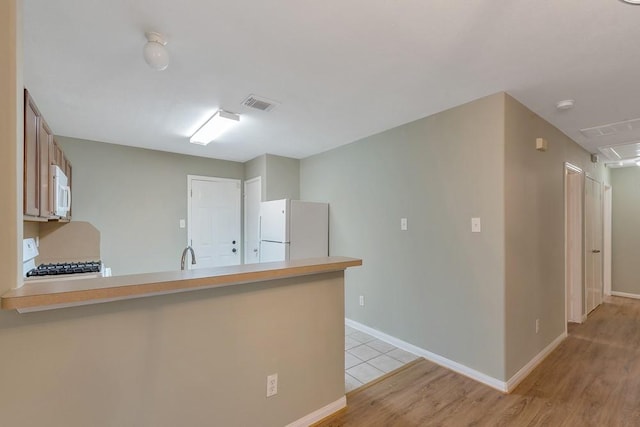 kitchen featuring sink, white appliances, kitchen peninsula, and light hardwood / wood-style flooring