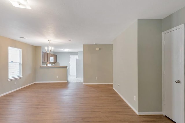 unfurnished living room with an inviting chandelier and light hardwood / wood-style flooring