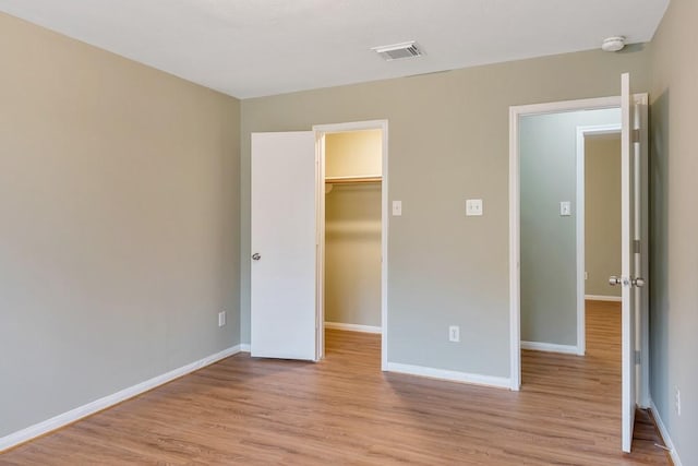 unfurnished bedroom with a closet, a walk in closet, and light hardwood / wood-style flooring