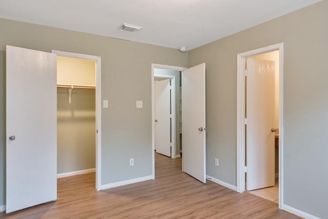 unfurnished bedroom with a spacious closet, a closet, and light hardwood / wood-style floors