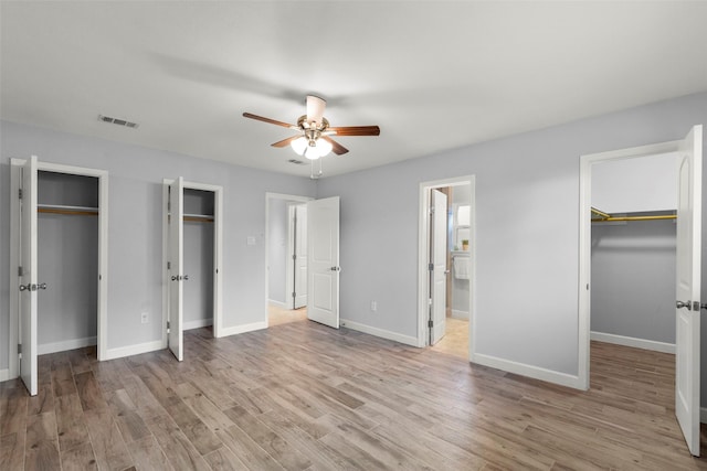 unfurnished bedroom with connected bathroom, ceiling fan, light hardwood / wood-style flooring, and multiple closets