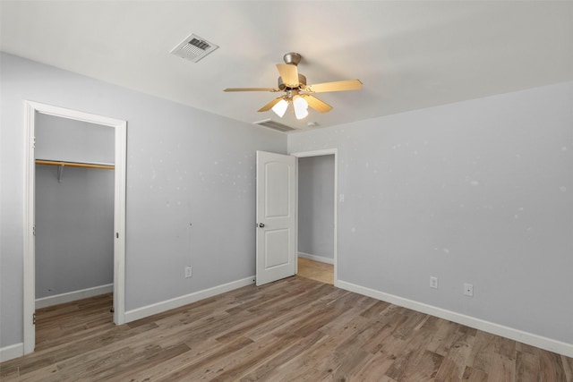 unfurnished bedroom featuring a closet, light hardwood / wood-style floors, a spacious closet, and ceiling fan