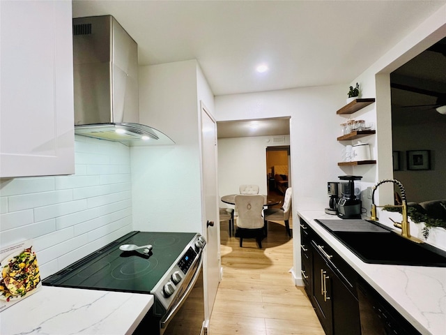 kitchen with open shelves, a sink, dark cabinetry, electric range oven, and wall chimney exhaust hood