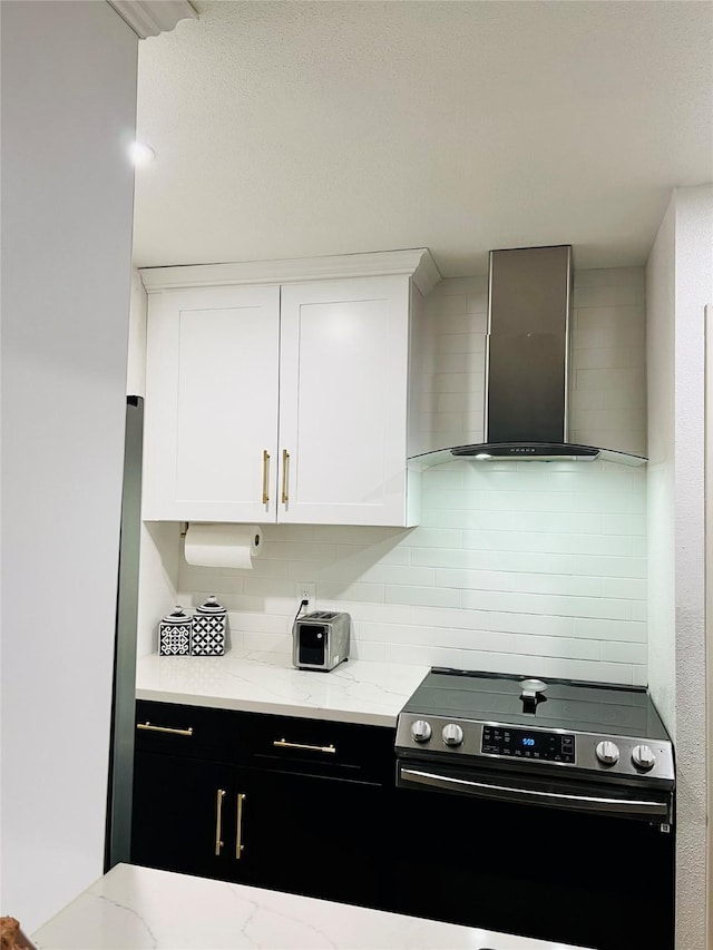 kitchen featuring electric range, tasteful backsplash, wall chimney exhaust hood, light stone countertops, and white cabinetry