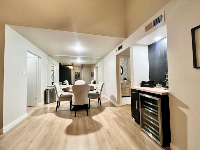 dining space with beverage cooler, light wood-type flooring, visible vents, and baseboards