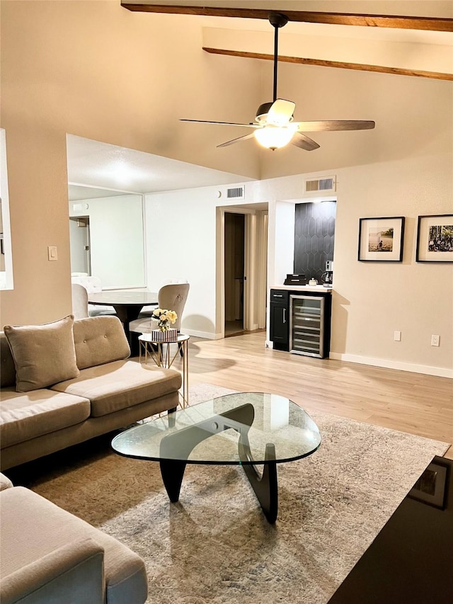 living area featuring light wood finished floors, beverage cooler, visible vents, baseboards, and vaulted ceiling with beams