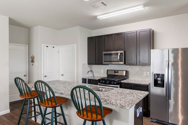 kitchen with light stone countertops, sink, stainless steel appliances, and an island with sink