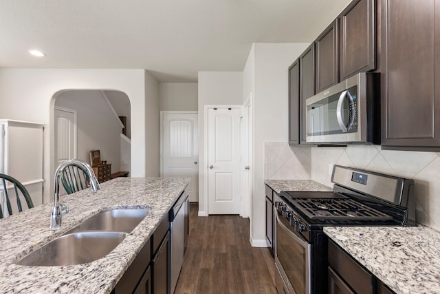 kitchen with light stone counters, sink, stainless steel appliances, and dark brown cabinets