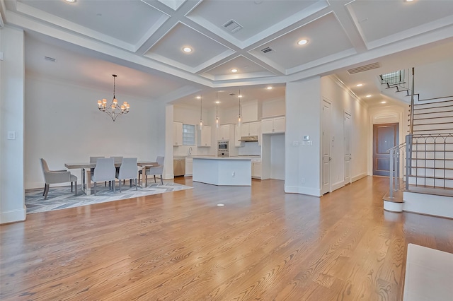 living room featuring coffered ceiling, light hardwood / wood-style flooring, ornamental molding, a notable chandelier, and beamed ceiling