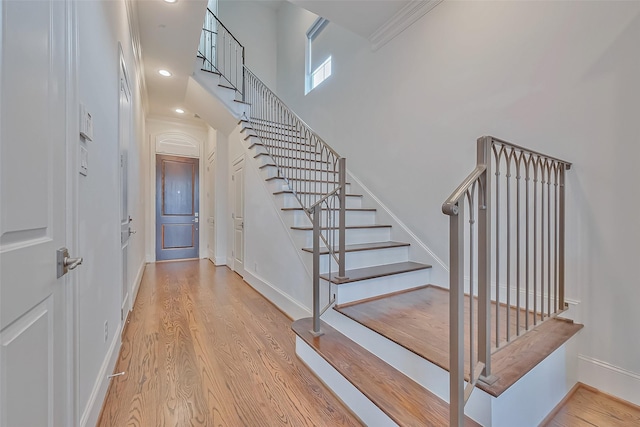 stairway with hardwood / wood-style flooring, ornamental molding, and a high ceiling