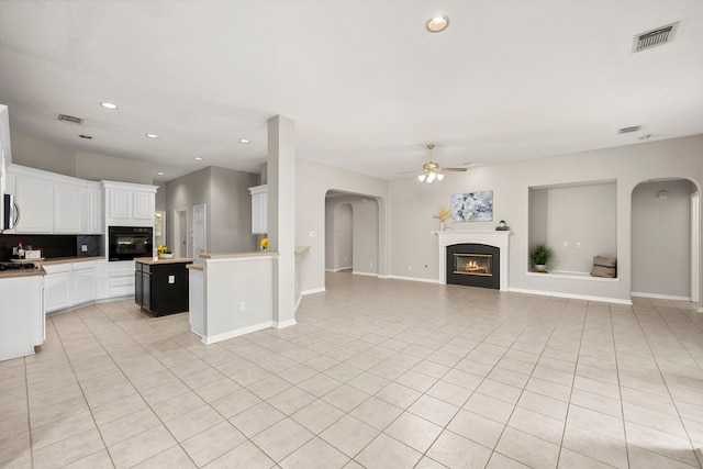 kitchen with a center island, oven, ceiling fan, light tile patterned flooring, and white cabinetry