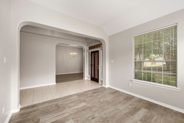 empty room with a chandelier, light hardwood / wood-style flooring, a wealth of natural light, and lofted ceiling