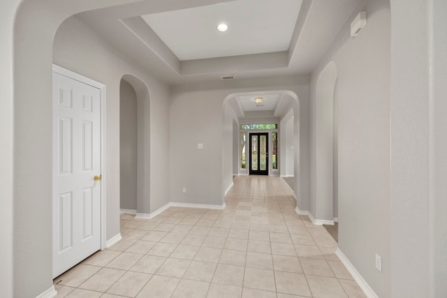 hall featuring a tray ceiling and light tile patterned floors