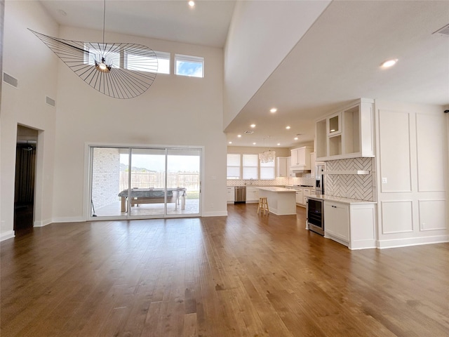 unfurnished living room with an inviting chandelier, beverage cooler, a high ceiling, and hardwood / wood-style flooring