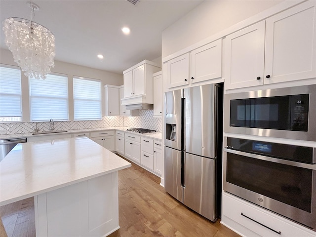 kitchen with white cabinetry, hanging light fixtures, stainless steel appliances, decorative backsplash, and a kitchen island