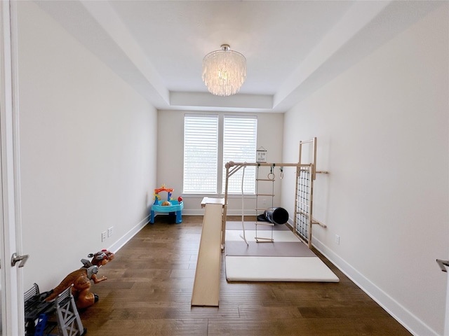 workout room with dark wood-type flooring, a tray ceiling, and a notable chandelier