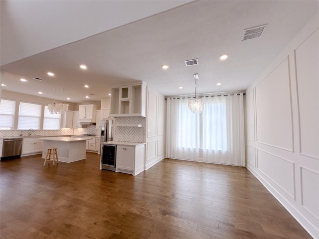 kitchen featuring white cabinetry, hanging light fixtures, a kitchen bar, a kitchen island, and appliances with stainless steel finishes