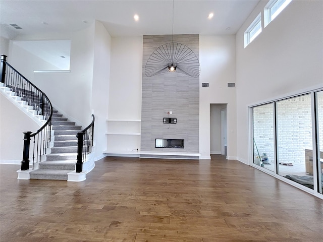 unfurnished living room featuring a fireplace, a towering ceiling, and dark wood-type flooring