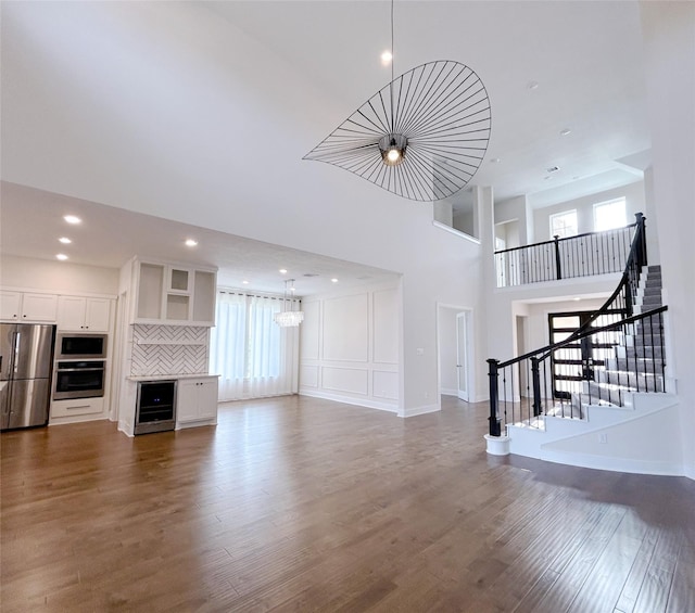 unfurnished living room featuring hardwood / wood-style floors, wine cooler, and a high ceiling