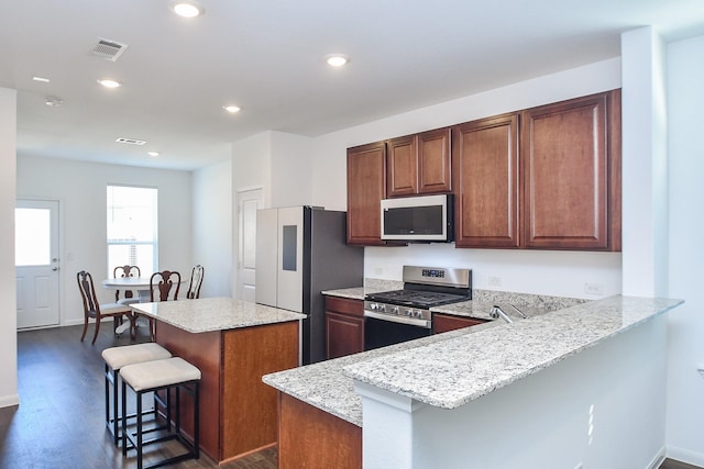 kitchen featuring a breakfast bar, appliances with stainless steel finishes, dark hardwood / wood-style floors, light stone countertops, and a kitchen island