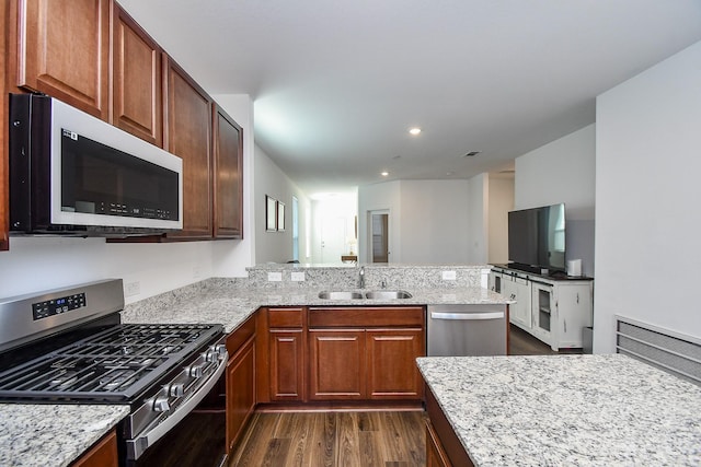 kitchen with appliances with stainless steel finishes, dark hardwood / wood-style floors, sink, light stone counters, and kitchen peninsula