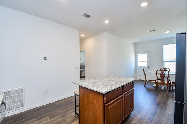 kitchen with stainless steel refrigerator, a kitchen breakfast bar, a center island, light stone counters, and dark hardwood / wood-style flooring