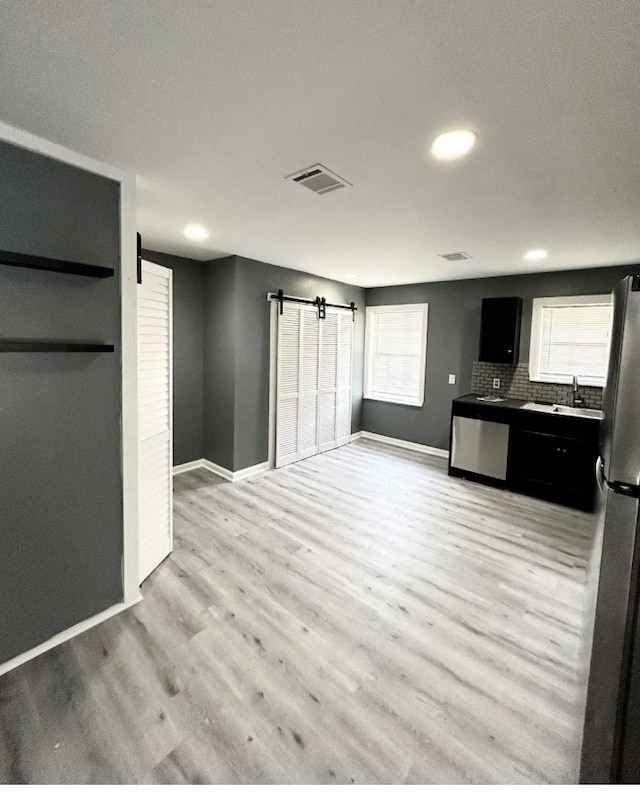 kitchen with a barn door, stainless steel appliances, light hardwood / wood-style flooring, and backsplash