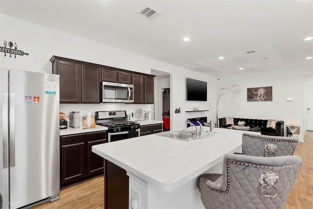 kitchen with dark brown cabinets, stainless steel appliances, light hardwood / wood-style flooring, a center island, and a breakfast bar area