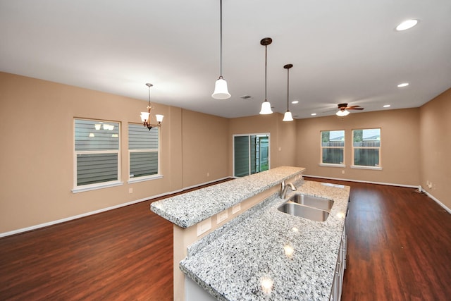 kitchen featuring light stone countertops, ceiling fan with notable chandelier, a kitchen island with sink, sink, and hanging light fixtures