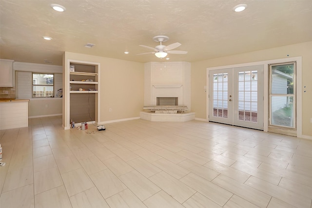 unfurnished living room featuring french doors, ceiling fan, built in features, a textured ceiling, and a fireplace