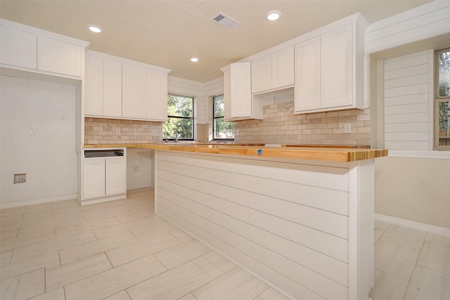 kitchen with a center island, backsplash, butcher block countertops, and white cabinetry