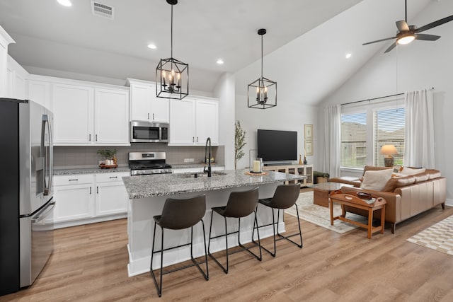 kitchen featuring stainless steel appliances, a kitchen island with sink, backsplash, and white cabinets