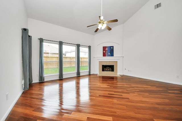 unfurnished living room with ceiling fan, high vaulted ceiling, a tiled fireplace, and hardwood / wood-style floors