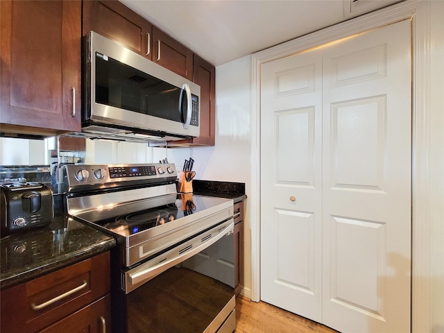 kitchen with light wood-type flooring, appliances with stainless steel finishes, and dark stone counters