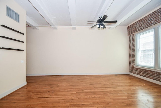 spare room featuring beam ceiling, ceiling fan, brick wall, and light wood-type flooring