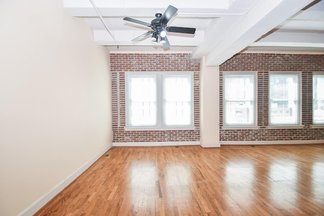 spare room with beam ceiling, light hardwood / wood-style flooring, ceiling fan, and brick wall