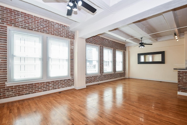 unfurnished living room featuring wood-type flooring, beam ceiling, and brick wall