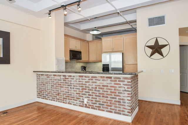 kitchen with dark stone counters, decorative backsplash, stainless steel fridge, light brown cabinetry, and kitchen peninsula