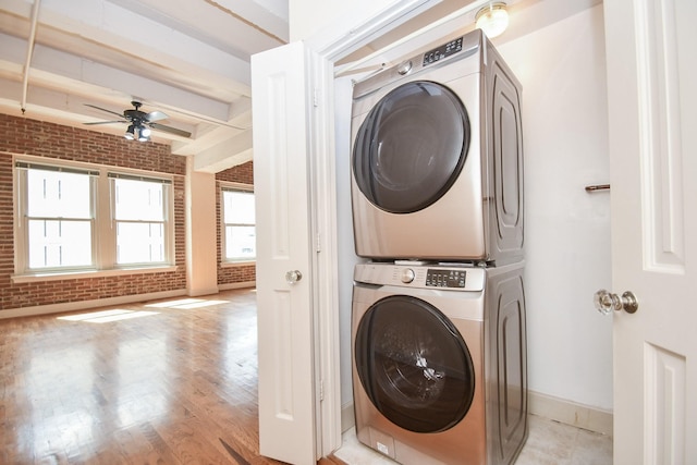 laundry area featuring ceiling fan, stacked washer / dryer, brick wall, and light hardwood / wood-style flooring