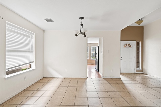 tiled spare room with a wealth of natural light and a chandelier