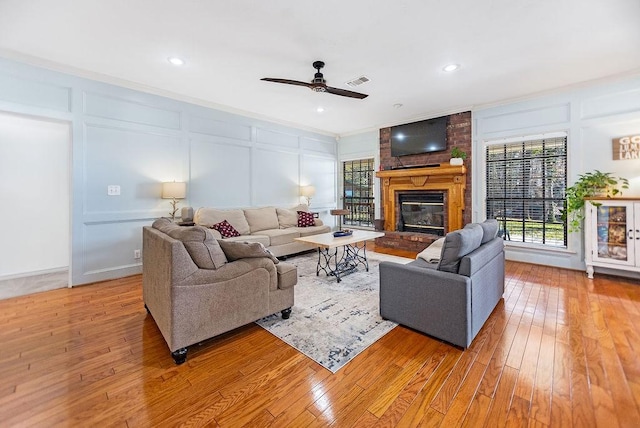 living room with ceiling fan, crown molding, a fireplace, and light hardwood / wood-style flooring