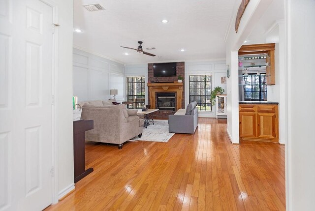 living room featuring a wealth of natural light, ceiling fan, light hardwood / wood-style flooring, and a brick fireplace