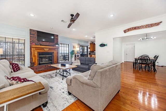 living room with a fireplace, ceiling fan with notable chandelier, hardwood / wood-style flooring, and ornamental molding