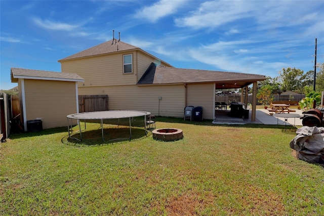 back of house with a fire pit, a trampoline, a patio, and a lawn