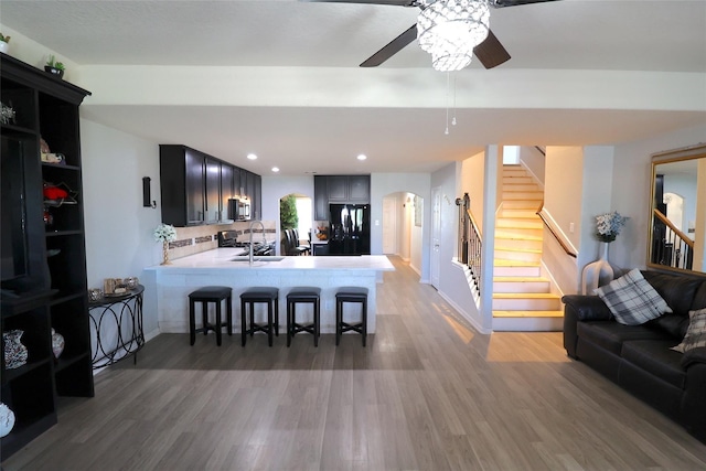 kitchen with ceiling fan, sink, black fridge, kitchen peninsula, and a breakfast bar area