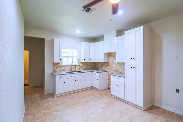 kitchen featuring white cabinets, decorative backsplash, light stone countertops, and sink