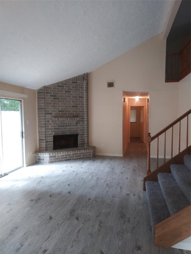 unfurnished living room with a textured ceiling, lofted ceiling, and a brick fireplace