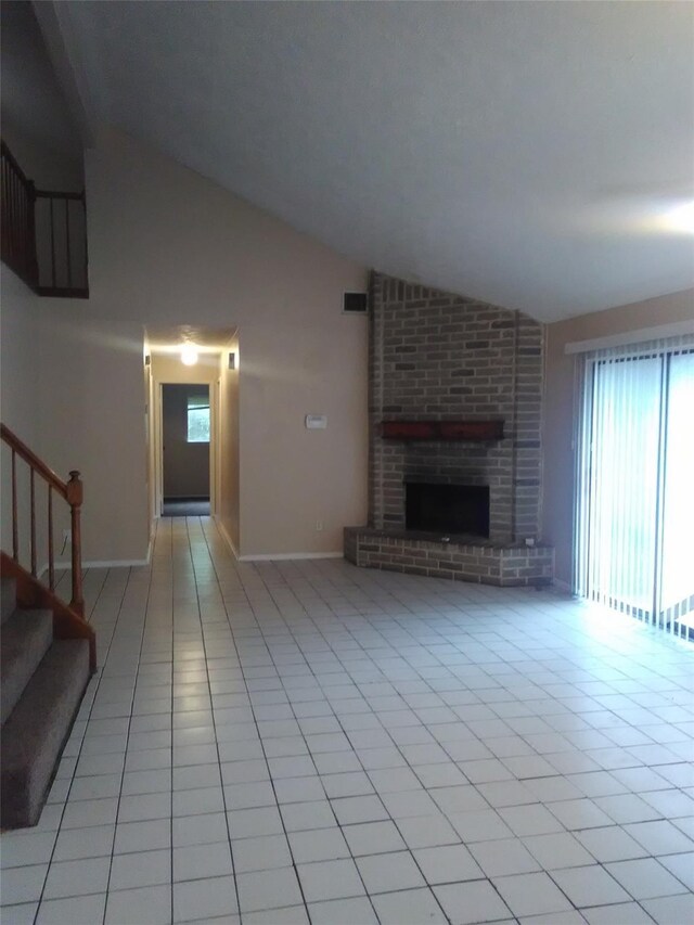 unfurnished living room featuring light tile patterned floors, a brick fireplace, lofted ceiling, and a healthy amount of sunlight