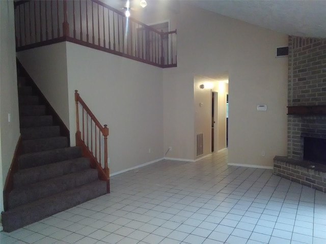 unfurnished living room featuring light tile patterned floors, a brick fireplace, and a high ceiling