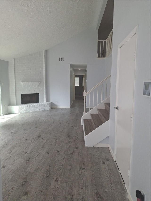 unfurnished living room with vaulted ceiling, visible vents, wood finished floors, a textured ceiling, and stairs